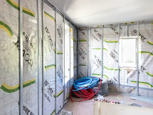 Intérieur en cours d'isolation, murs recouverts de pare-vapeur Isover Vario Xtra. Rouleaux de tuyaux bleus et rouges au sol. Un coup de pouce pour une isolation performante.