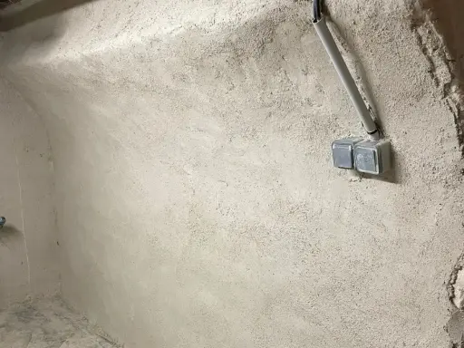 Mur brut avec prises électriques et tuyau, prêt pour enlever humidité maison. Un robinet bleu est visible à gauche.