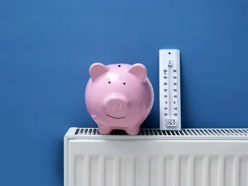 Tirelire rose sur un radiateur blanc, à côté d'un thermomètre. Pensez à l'entretien chaudière déductible impôts pour faire des économies.