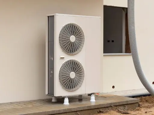 Une pompe à chaleur monobloc, avec ses deux ventilateurs, est installée à l'extérieur d'un bâtiment en construction.