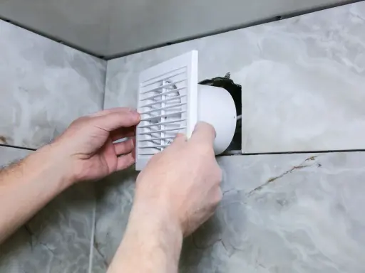 Installation d'une grille de ventilation VMC pour lutter contre la condensation dans une salle de bain carrelée.