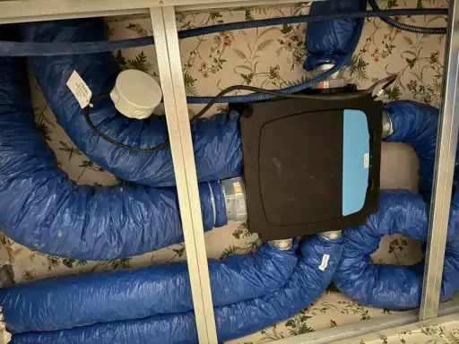 Système de ventilation centralisé avec un boîtier noir et bleu, entouré de conduits bleus isolés. Ce système VMC programmable assure un air sain.