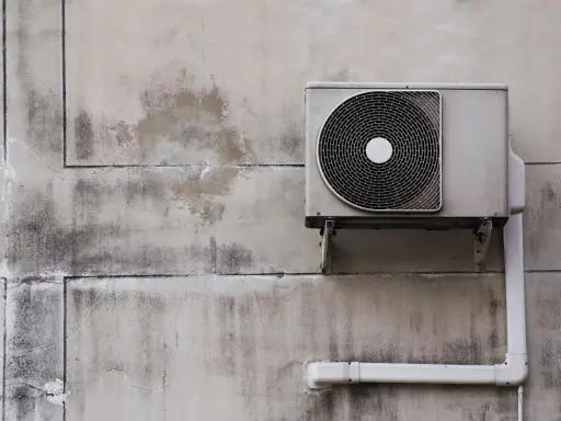 Unité extérieure de pompe à chaleur, sale et fissurée sur un mur décrépi. Avis négatif sur ce système.