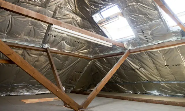 Isolation des combles 100m2 : vue d'un grenier en cours d'isolation avec matériaux réfléchissants et charpente bois.