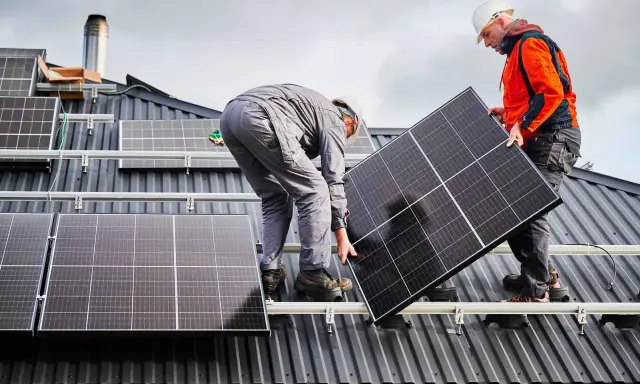 Deux ouvriers installent un panneau solaire sur un toit. La dimension du panneau solaire est adaptée pour maximiser la capture d'énergie.