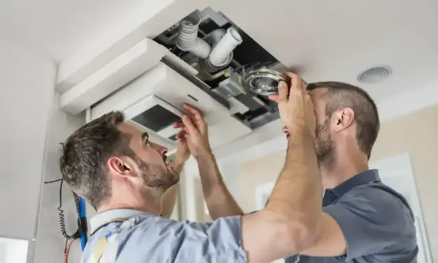 Deux hommes installent un système VMC dans un faux plafond. C'est là où se trouve la VMC dans une maison.