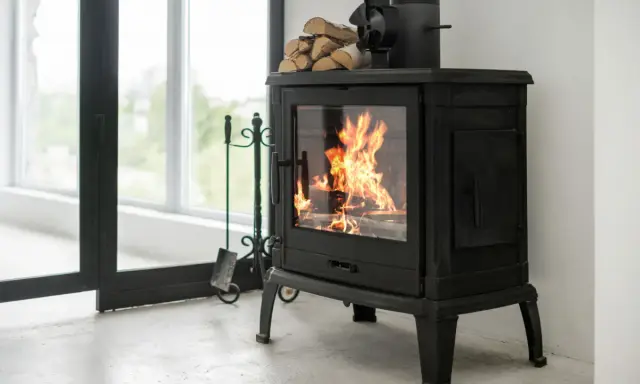 Un feu crépite dans ce cee poele a bois noir, prêt à réchauffer la pièce. Des bûches attendent sur le dessus.