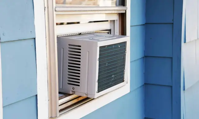 Climatisation réversible sans groupe extérieur installée dans une fenêtre. L'unité blanche est visible sur un mur bleu.