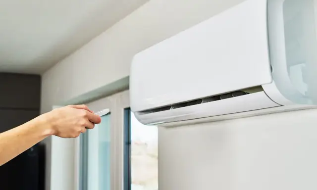 Main tenant utilise la télécommande pour régler le voyant clim.