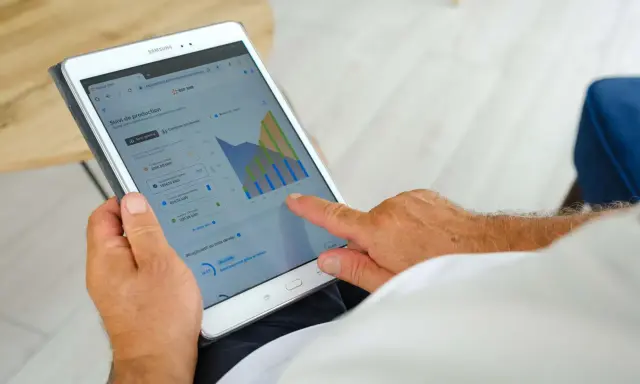 Homme consultant sa tablette : suivi de production solaire, consommation, autoconsommation et injection gratuite ENEDIS.