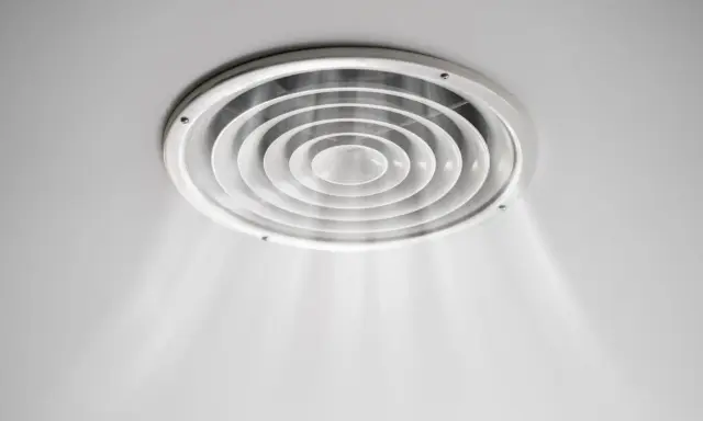 Grille de ventilation ronde au plafond, diffusant une légère brume. On dirait que la VMC pas assez puissante peine à renouveler l'air.