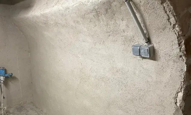 Mur brut avec prises électriques et tuyau, prêt pour enlever humidité maison. Un robinet bleu est visible à gauche.