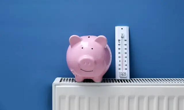 Tirelire rose sur un radiateur blanc, à côté d'un thermomètre. Pensez à l'entretien chaudière déductible impôts pour faire des économies.