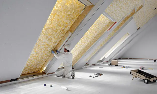 Un ouvrier installe un matériau isolant jaune texturé dans un grenier, assurant le meilleur isolant thermique pour la maison.