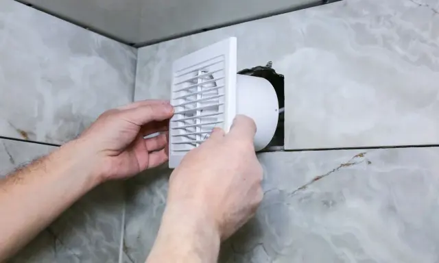 Installation d'une grille de ventilation VMC pour lutter contre la condensation dans une salle de bain carrelée.