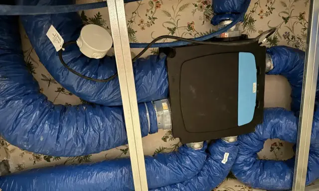 Système de ventilation centralisé avec un boîtier noir et bleu, entouré de conduits bleus isolés. Ce système VMC programmable assure un air sain.