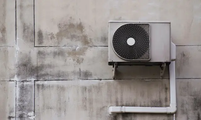 Unité extérieure de pompe à chaleur, sale et fissurée sur un mur décrépi. Avis négatif sur ce système.