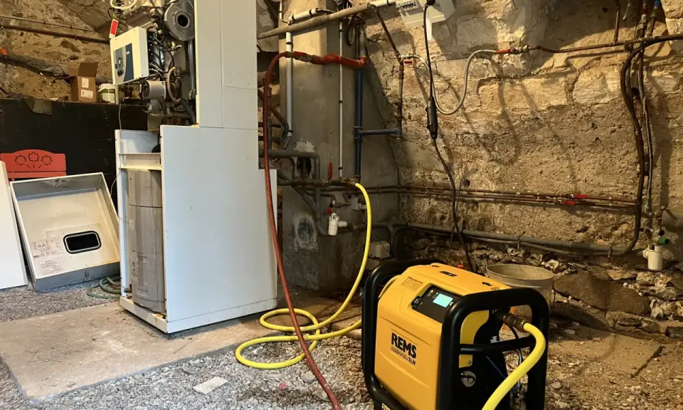 Un technicien effectue le desembouage d'une pompe à chaleur dans une chaufferie. L'équipement est relié à la chaudière par des tuyaux jaunes.