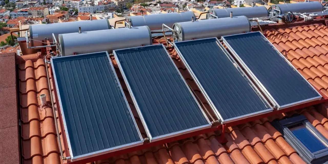Sur un toit de tuiles, plusieurs panneaux solaires thermiques sont installés, connectés à des chauffe-eau.