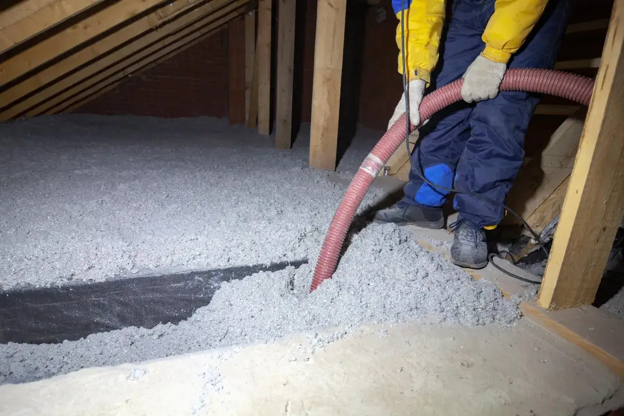 Pose d'isolation ouate de cellulose dans un grenier. Un ouvrier utilise un tuyau pour souffler le mat&eacute;riau isolant entre les poutres en bois.