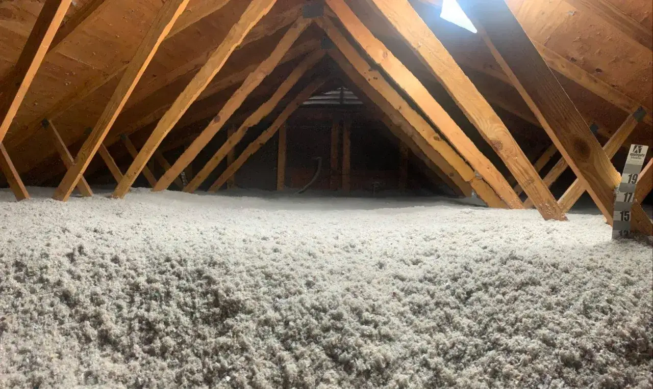 Vue d'un grenier avec une &eacute;paisse couche d'isolant souffl&eacute;, pr&ecirc;t pour l'isolation des combles. Les poutres en bois sont visibles au-dessus.