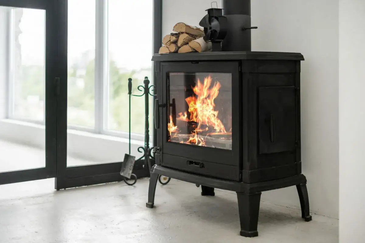 Un feu cr&eacute;pite dans ce cee poele a bois noir, apportant une ambiance chaleureuse. Des b&ucirc;ches attendent sur le dessus.