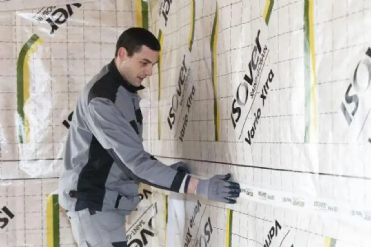 Un ouvrier pose une membrane pour l'isolation mur intérieur. Le matériau est marqué 