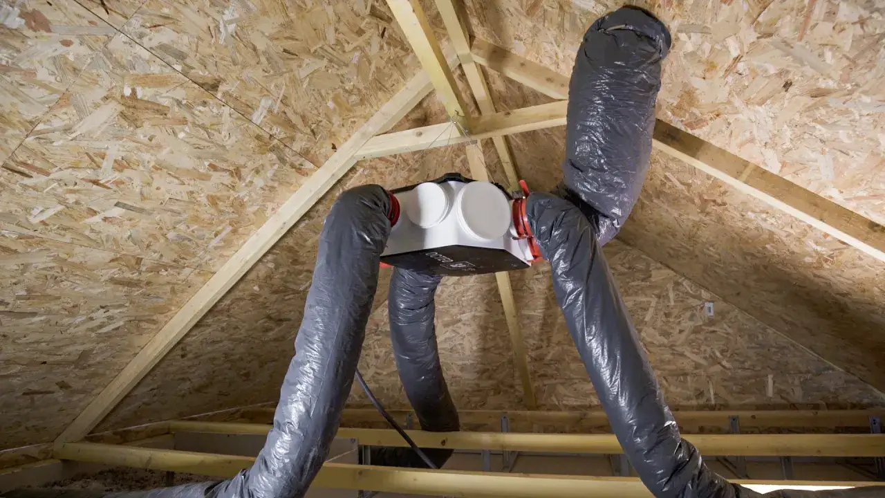 Installation d'une VMC simple flux dans un grenier. Le caisson blanc est suspendu, relié à des gaines grises isolées.