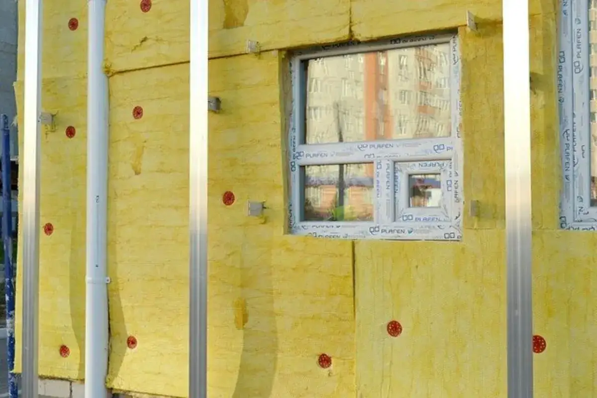 Isolation jaune sur un mur ext&eacute;rieur, avec des montants m&eacute;talliques et une fen&ecirc;tre. La pose de ce mat&eacute;riau assure une excellente r&eacute;sistance thermique du bois.