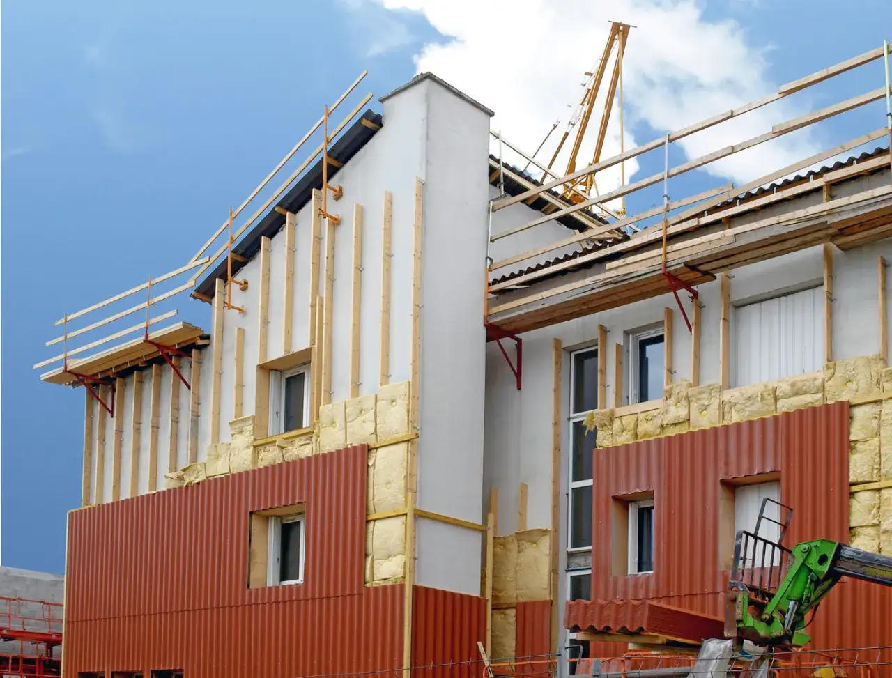 Chantier de construction : pose de l'isolant et des bardages pour une isolation par l'extérieur. Grue et échafaudages visibles.