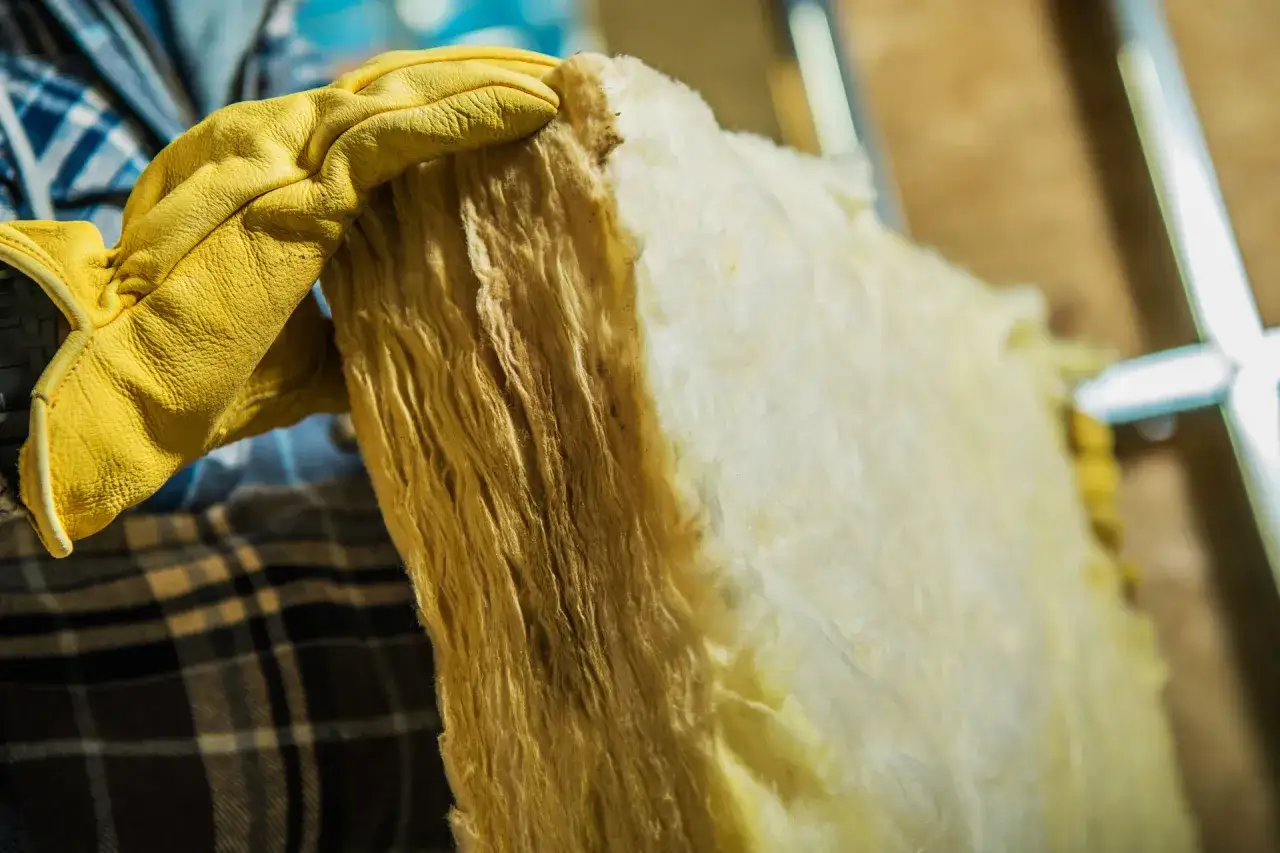 Main isolante en laine de verre, prêt à être recyclé à la déchetterie. Un travailleur porte des gants jaunes pour manipuler ce matériau.