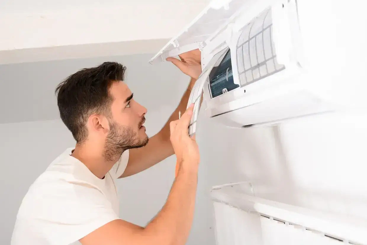 Un homme nettoie le filtre d'une climatisation r&eacute;versible. Demandez le tarif entretien clim r&eacute;versible pour un air pur.