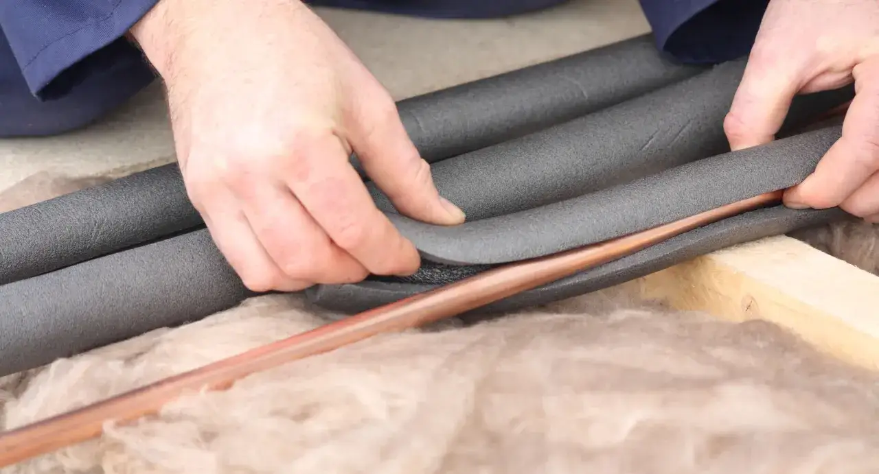 Mains de personne pla&ccedil;ant une gaine isolante pour isoler un tuyau de chauffage en cuivre.