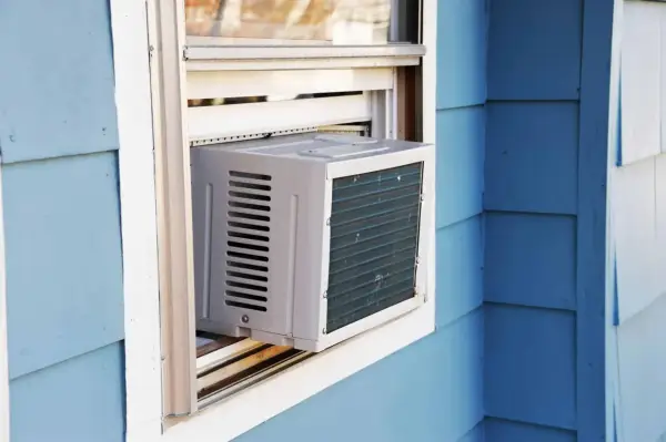 Climatisation réversible sans groupe extérieur installée dans une fenêtre. L'unité blanche est visible sur un mur bleu.