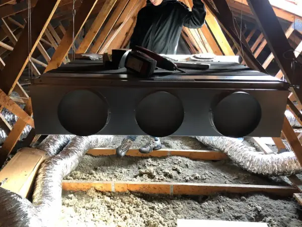 Installation d'un système de climatisation gainable dans un grenier. Un technicien est visible, prêt pour l'entretien.