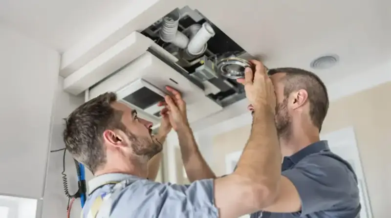 Deux hommes installent un système VMC dans un faux plafond. C'est là où se trouve la VMC dans une maison.