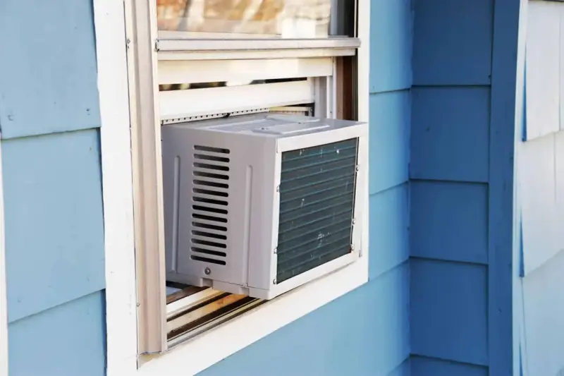Climatisation réversible sans groupe extérieur installée dans une fenêtre. L'unité blanche est visible sur un mur bleu.